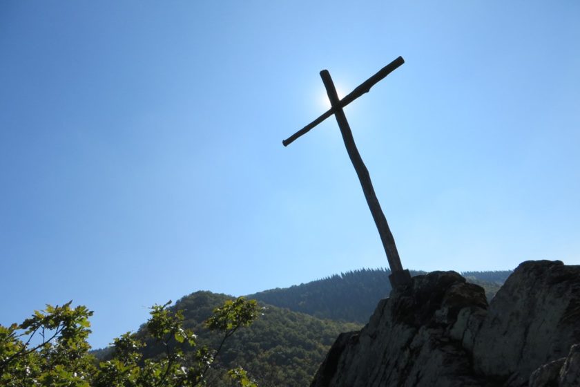 Ein karges Holzkreuz vor strahlendblauem Himmel auf einer Felsengruppe über dem Ahrtal