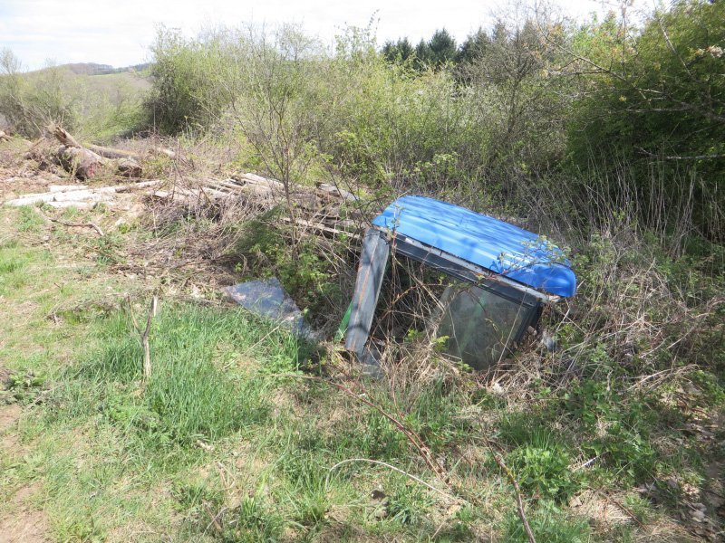 Die Fahrerkabine eines Traktors, einfach abgeladen, wird langsam vom Gras überwuchert.